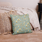 Turquoise & Gold Magnolia Dreams decorative pillow featuring magnolias, hummingbirds and butterflies in a muted gold tone styled against a cosy sofa and pillows in a neutral, beige colour