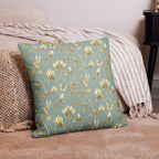 Turquoise & Gold Magnolia Dreams decorative pillow featuring magnolias, hummingbirds and butterflies in a muted gold tone styled against a cosy sofa and pillows in a neutral, beige colour