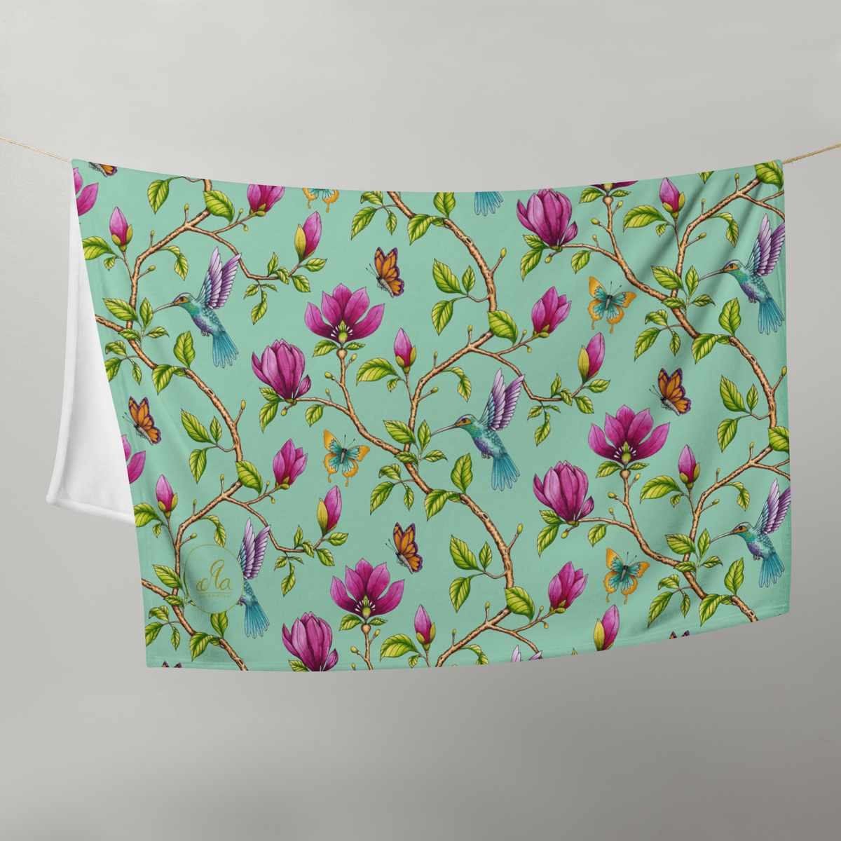 Magnolia Dreams throw blanket in Vista Blue, hanging on a line and featuring pink magnolia blossoms, colorful hummingbirds, butterflies and green leaves