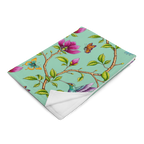 Magnolia Dreams throw blanket in Vista Blue, folded to showcase pink magnolia blossoms, colorful hummingbirds, butterflies and green leaves