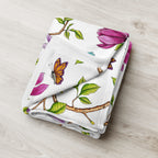 Close-up of a Magnolia Dreams throw blanket featuring pink magnolia blossoms, green leaves and colorful butterflies on a white background