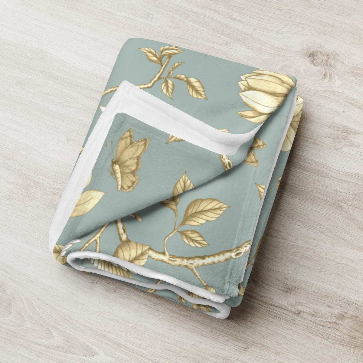 Folded Magnolia Dreams Gilded Garden throw blanket in Turquoise & Gold, featuring delicate golden magnolia blossoms, leaves and butterflies