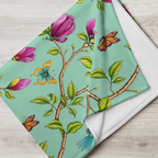 Close-up of a Magnolia Dreams throw blanket in Vista Blue, featuring pink magnolia blossoms, colorful butterflies and green leaves