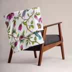 Magnolia Dreams throw blanket draped over a chair, featuring pink magnolia blossoms, colorful hummingbirds, butterflies and green leaves on a white background