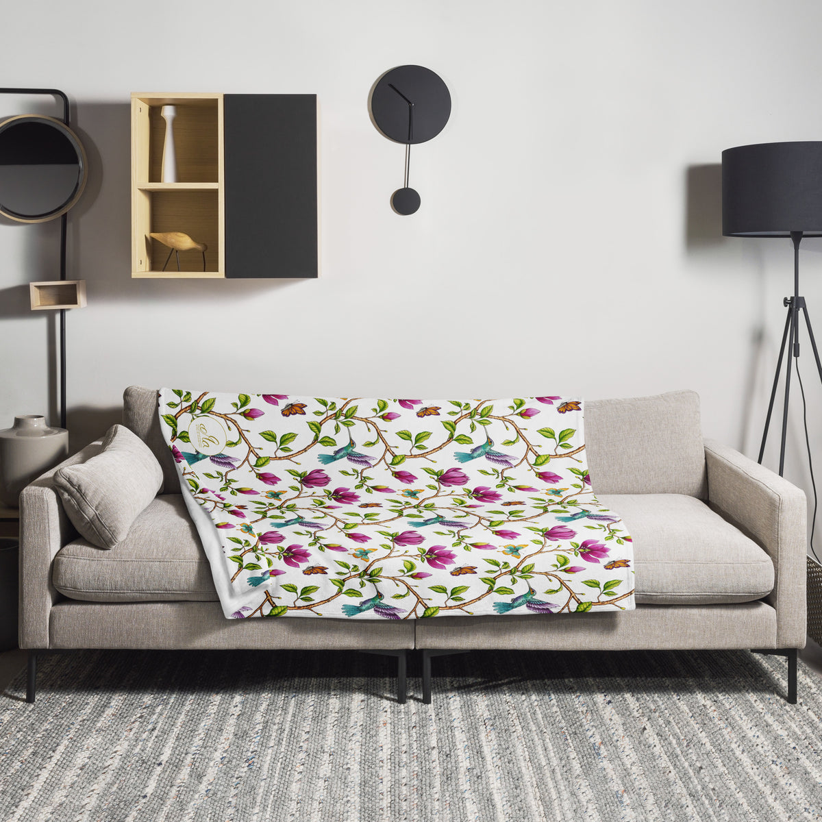 Garden of Eden throw blanket draped over a sofa, featuring pink magnolias, colorful hummingbirds and butterflies on a white background
