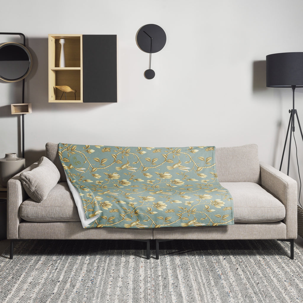 Magnolia Dreams Gilded Garden throw blanket in turquoise and gold, draped over a sofa