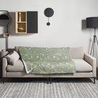 Magnolia Dreams Gilded Garden throw blanket in turquoise and gold, draped over a sofa