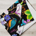 Close-up of a Garden of Eden throw blanket showing a colorful kingfisher, magnolia flowers, berries and green leaves against a black background
