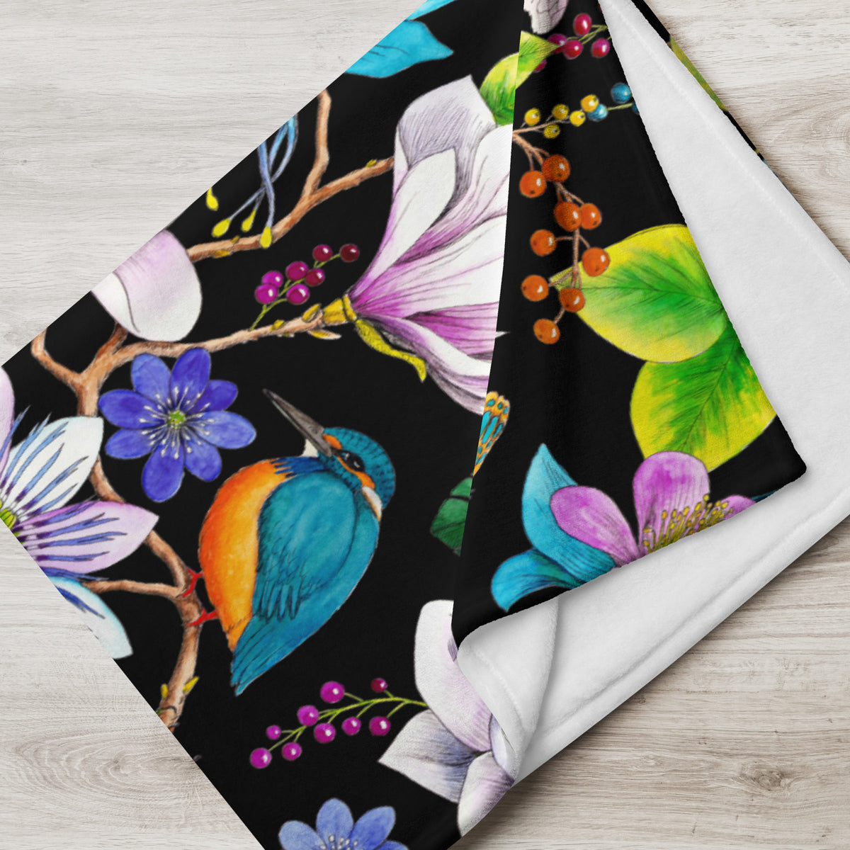 Close-up of a Garden of Eden throw blanket showing a colorful kingfisher, magnolia flowers, berries and green leaves against a black background