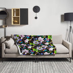 Garden of Eden throw blanket draped over a sofa, featuring colorful exotic flowers, kingfishers, butterflies and lush green leaves on a black background