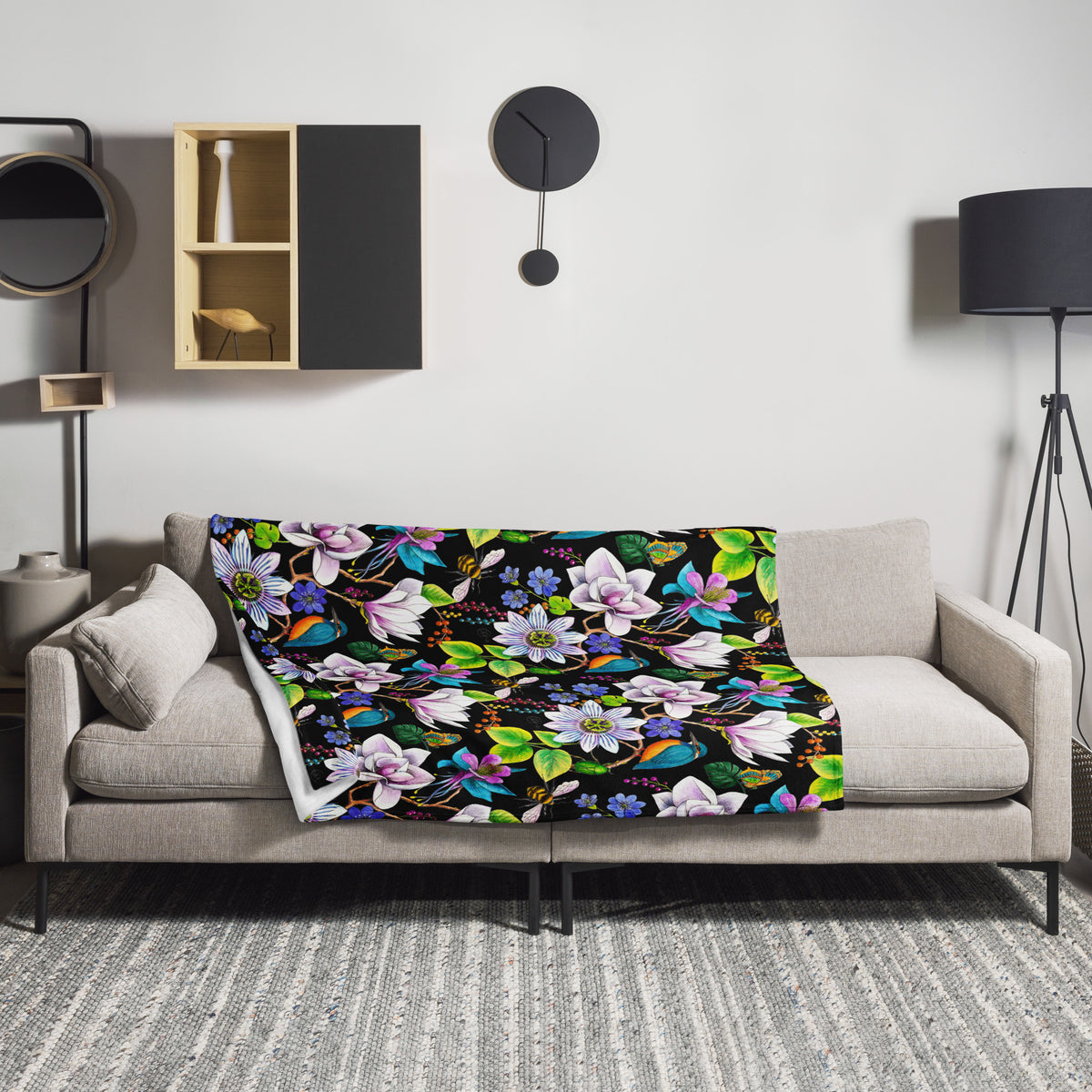 Garden of Eden throw blanket draped over a sofa, featuring colorful exotic flowers, kingfishers, butterflies and lush green leaves on a black background