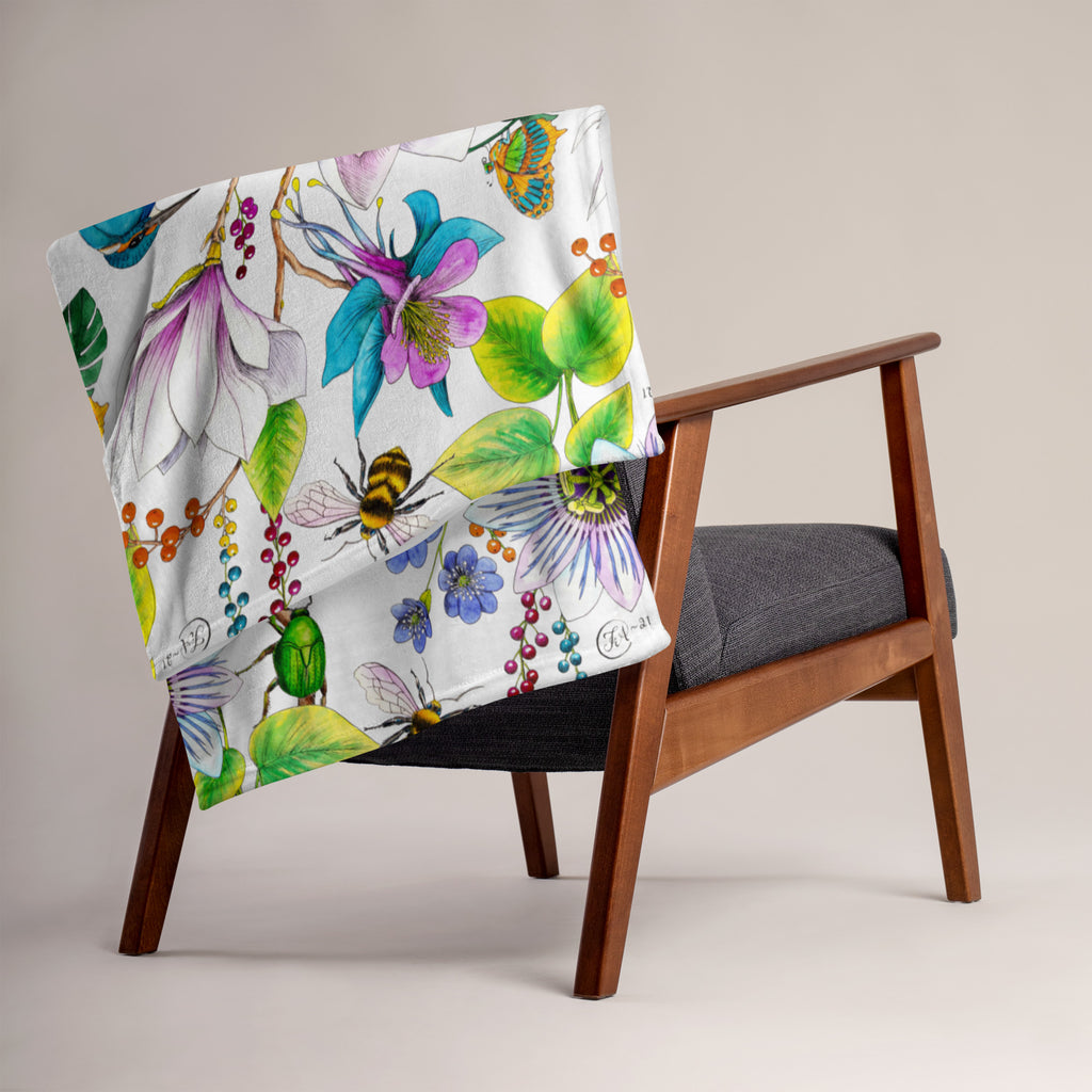 Garden of Eden throw blanket draped over a chair, featuring colorful exotic flowers, green leaves, a kingfisher and bumblebees