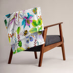 Garden of Eden throw blanket draped over a chair, featuring colorful exotic flowers, green leaves, a kingfisher and bumblebees