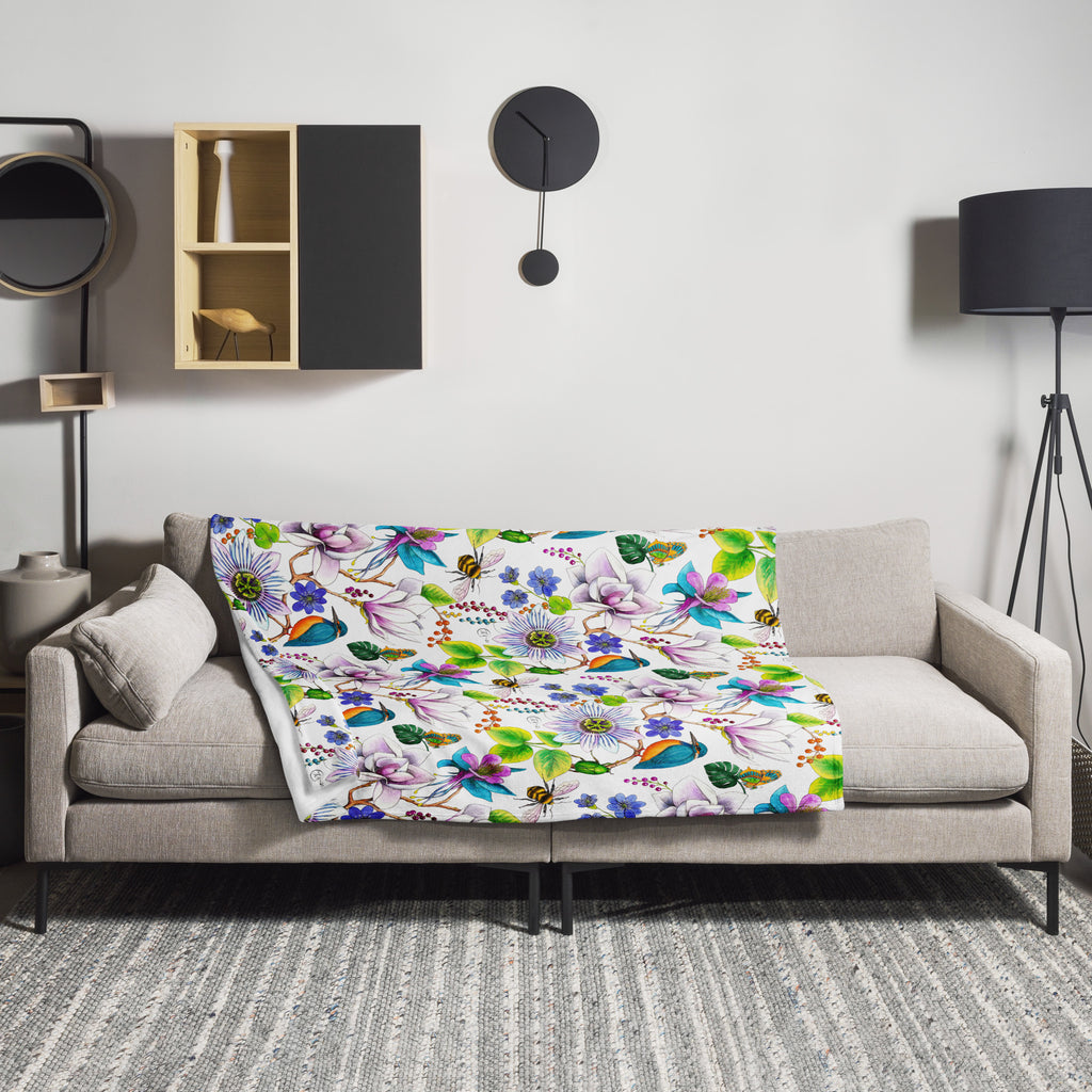 Garden of Eden throw blanket draped over a sofa, featuring colorful exotic flowers, a kingfisher and a bumblebee