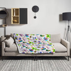 Garden of Eden throw blanket draped over a sofa, featuring colorful exotic flowers, a kingfisher and a bumblebee