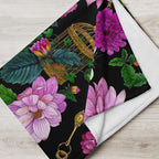 Close-up of a throw blanket featuring the Dahlia Garden pattern, showing colorful flowers, leaves and a decorative birdcage