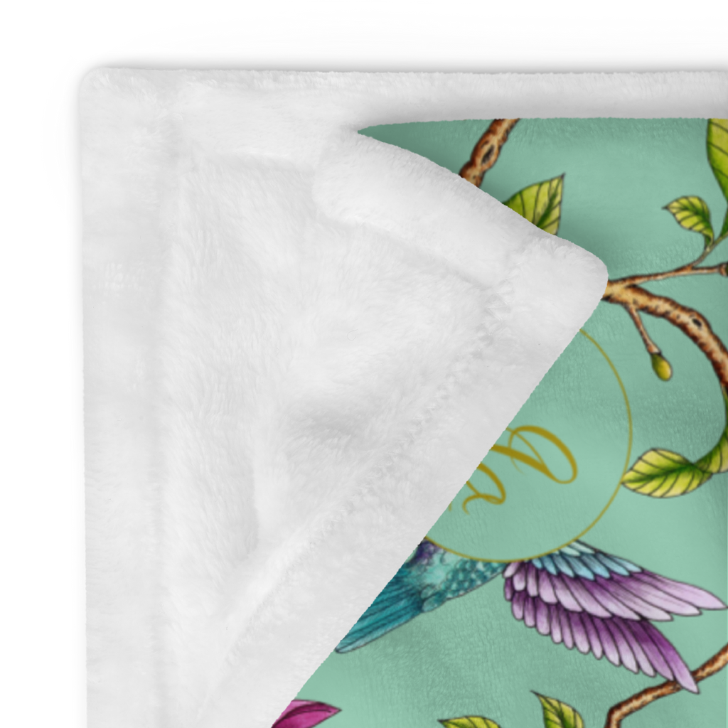 Close-up of a Magnolia Dreams throw blanket with pink magnolia blossoms, green leaves and colorful hummingbirds on a white background
