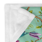 Close-up of a Magnolia Dreams throw blanket with pink magnolia blossoms, green leaves and colorful hummingbirds on a white background