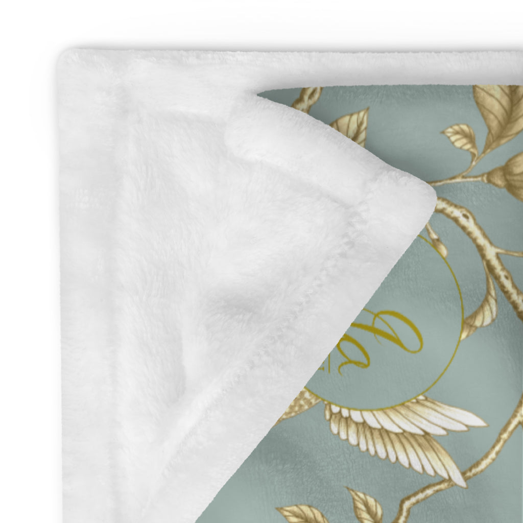 Close-up of a Magnolia Dreams Gilded Garden throw blanket in Turquoise & Gold, featuring golden magnolia branches and a hummingbird