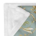 Close-up of a Magnolia Dreams Gilded Garden throw blanket in Turquoise & Gold, featuring golden magnolia branches and a hummingbird